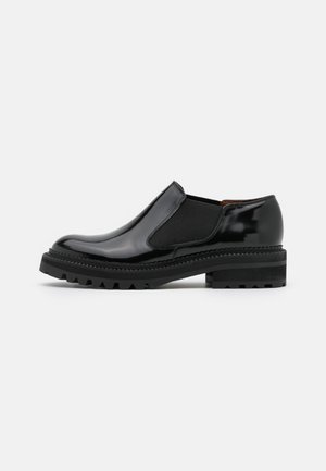 Chaussure noire en cuir brillant à enfiler avec panneaux élastiques latéraux, semelle crantée épaisse et petit talon superposé, vue du côté extérieur.