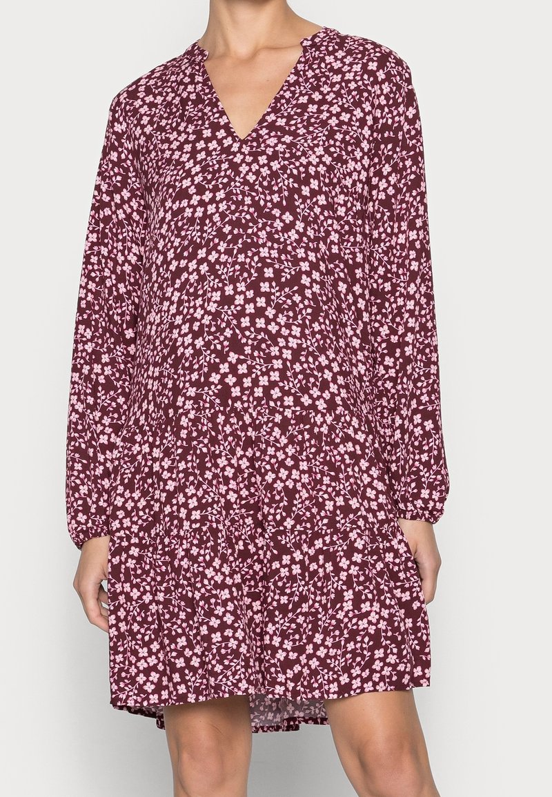 Vestido burdeos con escote en V, mangas largas y falda de volantes. Presenta un patrón floral rosa en toda su extensión, realizado en una tela ligera.