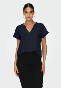 Blusa blu navy a maniche corte con scollatura a V e tessuto texturizzato, abbinata a una gonna nera aderente a coste. Design minimalista, senza motivi.