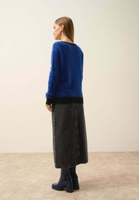 Modrý pletený svetr s černými detaily, kombinovaný s dlouhou černou denimovou sukní a modrými botami na podpatku. Hladké textury a uvolněný střih.