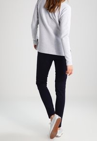 Haut gris à manches longues associé à un pantalon slim bleu marine foncé. Chaussures blanches avec une semelle texturée. Design simple et décontracté avec des accents minimaux.
