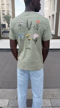 Šviesiai žalia marškinėliai, kurių nugarinėje pusėje pavaizduotos spalvingos siuvinėjamos gėlės. Derinami su šviesiai mėlynomis džinsais, audinys atrodo minkštas ir tekstūruotas.