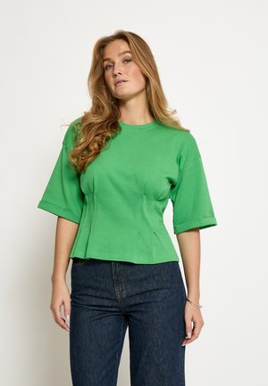 Grøn t-shirt med korte ærmer og rund hals i glat bomuldsmateriale, figursyet ved taljen med sidesømme, kombineret med mørke jeans.