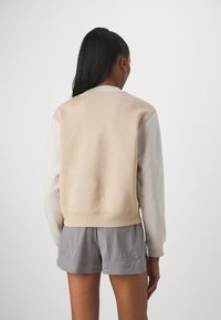 Béžová a světle šedá mikina s kulatým výstřihem, řaseným lemem a manžetami na rukávech. Hladká textury s kontrastními barevnými bloky na rukávech.