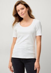 Weiße Kurzarm-T-Shirt aus weichem Stoff, mit rundem Halsausschnitt und figurbetontem Schnitt. Kombiniert mit dunkelblauen Jeans.