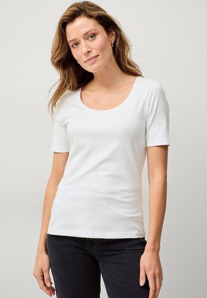 Witte T-shirt met korte mouwen van zacht stof, met een ronde halslijn en een aangesloten ontwerp. Gecombineerd met donkere jeans.