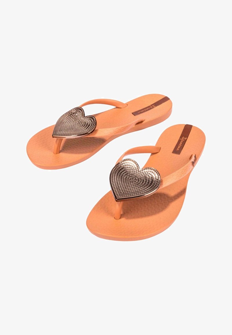 Chanclas naranjas con una suela texturizada, que presentan un adorno metálico con forma de corazón decorado con diamantes de imitación en la tira.
