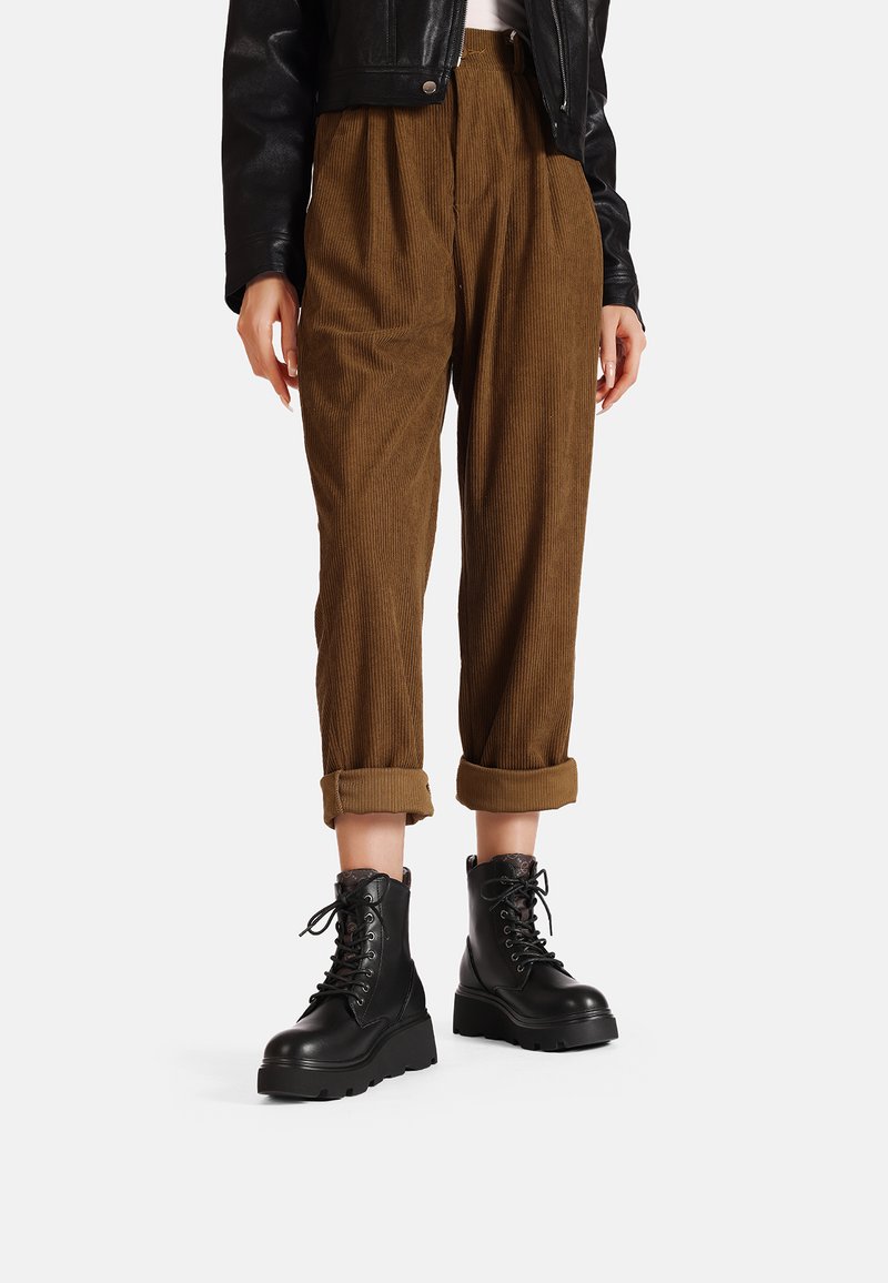 Pantaloni in velluto a coste marroni con vestibilità rilassata e orli arrotolati, abbinati a stivali da combattimento neri con lacci e suola spessa. Giacca di pelle nera.