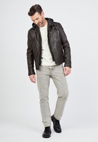 Ruskea nahkatakki harmaalla hupparivuorilla, vetoketjukiinnitys ja sivutaskut. Puettu vaalean neuleen päälle, yhdistettynä vaaleanharmaisiin farkkuihin ja mustiin saappaisiin.