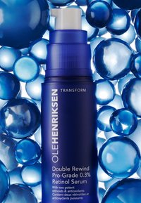 Niebieska butelka pompy OLEHENRIKSEN Double Rewind Retinol Serum otoczona różnymi niebieskimi żelowymi kulkami, charakteryzująca się eleganckim designem i błyszczącą teksturą.