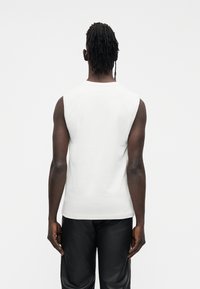 Wit mouwloos katoenen shirt met een ronde hals, gecombineerd met zwarte broek met structuur. Eenvoudig ontwerp, minimale details.