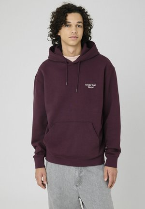 Sweat à capuche bordeaux avec une poche avant, une capuche à cordon de serrage et le texte « Create Your World » en blanc sur la poitrine ; tissu doux et coupe décontractée.