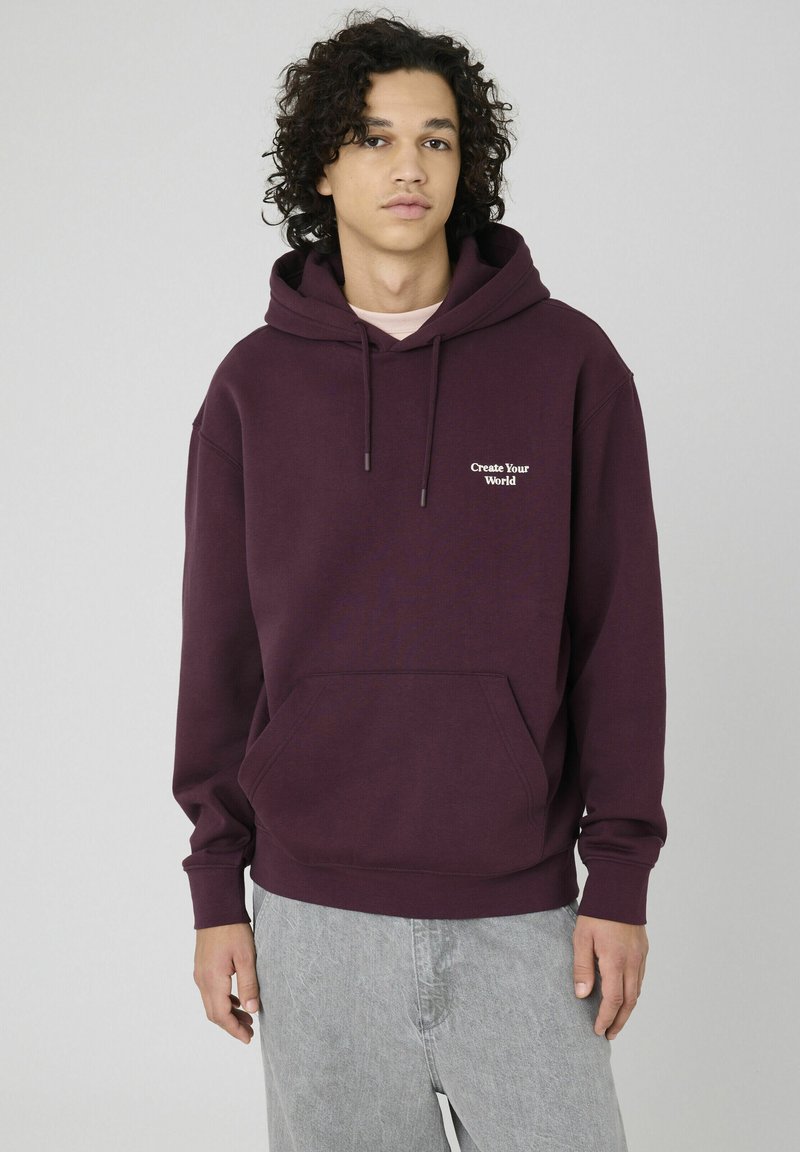 Sweat à capuche bordeaux avec une poche avant, une capuche à cordon de serrage et le texte « Create Your World » en blanc sur la poitrine ; tissu doux et coupe décontractée.
