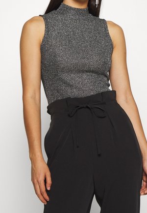 Ærmeløs grå striktop med høj hals kombineret med højtaljede sorte bukser med bælte bundet i taljen.