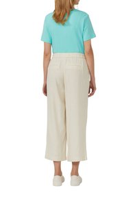 Una maglietta a maniche corte turchese abbinata a pantaloni larghi di colore crema, con una vestibilità comoda e una vita elasticizzata, vista da dietro.