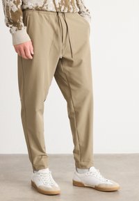 Beiga tapered-byxor i mjukt tyg med elastisk midja och dragsko. Kombineras med vita sneakers med gummisula.