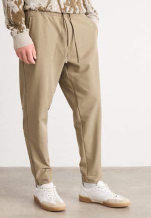 Beiga tapered-byxor i mjukt tyg med elastisk midja och dragsko. Kombineras med vita sneakers med gummisula.