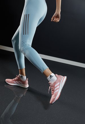 Chaussures de sport roses avec des rayures blanches, assorties à des leggings bleu clair avec des rayures grises. La surface est sombre et brillante.