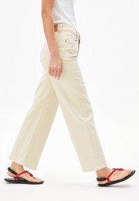 Brede, crèmekleurige jeans van katoen, met voorzakken en een knoopsluiting. Gecombineerd met zwarte sandalen met rode straps.