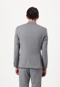 Veste de costume grise avec un design structuré, un tissu texturé et des revers crantés. La veste comporte une fente simple et des accents de poignet boutonné.