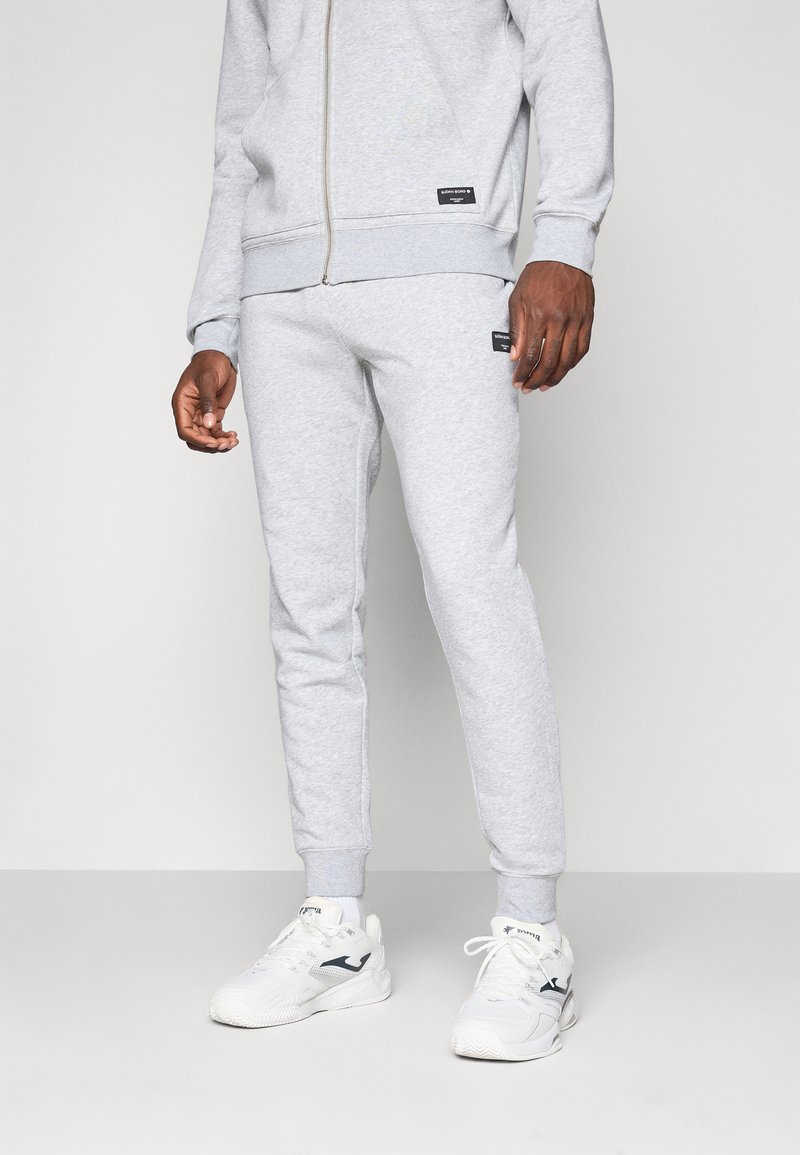 Grå bomuldsblandet træningsdragt med en lynlåsjakke og tapered bukser med ribbede manchetter, der komplementeres af hvide sneakers med mørke accenter.