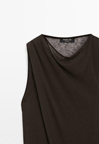 Haut sans manches marron foncé avec un large col rond, en tissu léger légèrement transparent, suspendu sur un fond blanc.