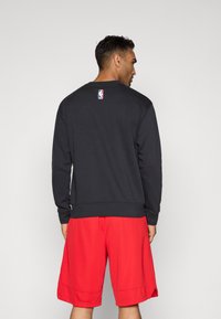 NBA džemperis melnā kokvilnā, ar apaļu kaklu, ribot�ām rokas piedurknēm, aizmugurē ar logo. Kombinēts ar sarkaniem sporta šortiem, teksturēta auduma, ar elastīgu jostu.