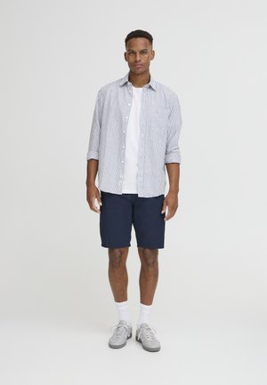 Stribet skjorte i hvid og blå, båret over en hvid T-shirt, parret med navy shorts. Afsluttet med grå sneakers og hvide sokker.