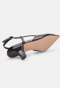 Črne lakirane slingback pumpe s koničastim prstom, nizko blok peto in tankim pasom, pritrjenim z zlatim sponko. Gladka tekstura.