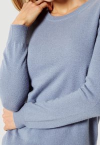 Pull bleu clair à manches longues en tricot doux avec un col rond et des poignets côtelés, présentant une texture lisse.