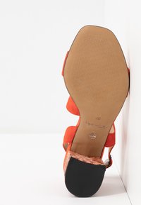 Sandale avec des brides orange, bout carré et talon bloc tissé, vue depuis la semelle sur fond blanc.