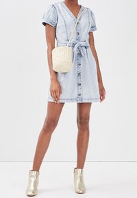 Light blue denim dress with short puff sleeves, v-neckline, front buttons, and tie waist. Paired with a cream woven bag and metallic ankle boots.
