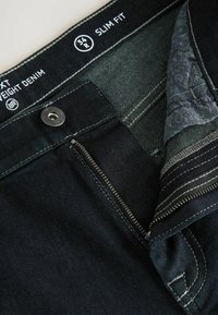 Jeans slim fit din denim închis la culoare cu fermoar, închidere cu buton metalic și căptușeală interioară cu model. Prezintă cusături contrastante și detalii cu etichete.