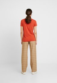 Červené bavlněné tričko s krátkým rukávem, spárované s širokými kalhotami s károvaným vzorem v béžové barvě. Kalhoty mají kostkovaný vzor a uvolněný střih.