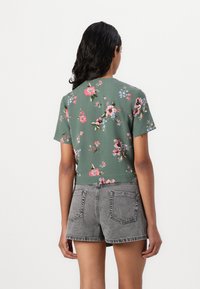Top verde a maniche corte con stampa floreale, abbinato a pantaloncini in denim grigi. Caratterizzato da un collo rotondo e un design corto.