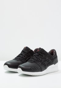 Svarta sportskor med ovandel i läder och tyg, med en texturerad svart snörningsdel och svart sula med vita accenter. Mönstrad innersula.