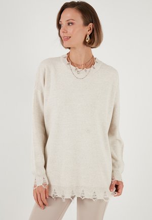 Maglione color crema con collo e maniche a coste, caratterizzato da un dettaglio di orlo sfrangiato. Texture morbida, vestibilità rilassata e maniche lunghe.