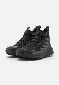 Scarpe sportive nere con design alta, tomaia in rete, accenti testurizzati e suola robusta per la trazione. Dettagli riflettenti lungo i lati.