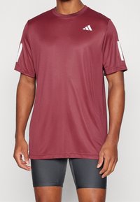 Camiseta deportiva en color burdeos, fabricada con una tela ligera que absorbe la humedad. Presenta detalles en blanco en las mangas y un logo en el pecho.