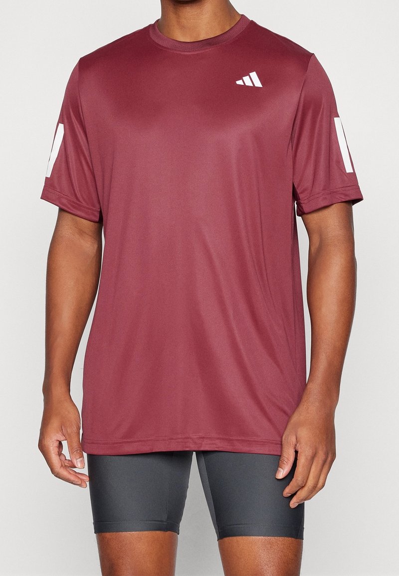 Camiseta deportiva en color burdeos, fabricada con una tela ligera que absorbe la humedad. Presenta detalles en blanco en las mangas y un logo en el pecho.