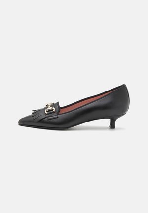 Chaussure en cuir noir à talon kitten avec bout pointu, détail frangé à l'avant et accent de boucle dorée, présentée sur un fond blanc.