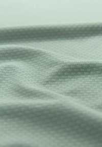 Jasnozielony materiał teksturowany z subtelnym geometrycznym wzorem, z delikatnymi fałdami podkreślającymi jego gładką powierzchnię i lekką jakość.