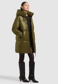 Olive roheline puhv coat kõrge kraega ja lukuga. Kanga läikega viimistlus, ülekaalulised proportsioonid ja elastsed mansetid.