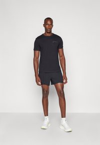 Tricou sportiv scurt negru cu mâneci scurte și un logo în partea stângă sus, asortat cu pantaloni scurți negri și încălțăminte sportivă albă. Design simplu, textură netedă.