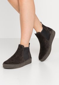 Bottes chelsea en daim noir avec des panneaux latéraux élastiques et une semelle en caoutchouc texturée, présentant un bout arrondi et un design minimaliste.