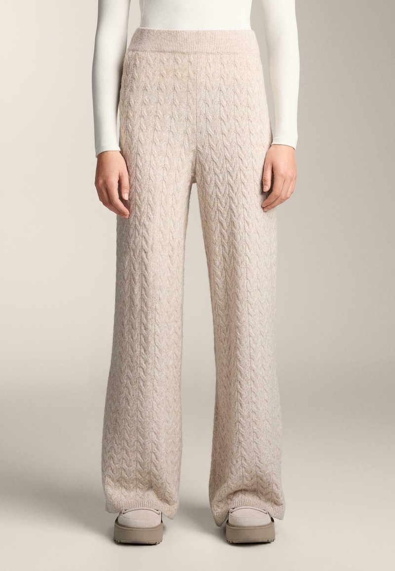 Svetlobéžové pletené široké nohavice s textúrovaným vrkočovým vzorom a rebrovaným pásom, vyrobené z mäkkej, pohodlnej látky s voľným strihom.