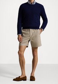 Námořnický svetr s kabelovým pletením, pruhovaná košile s límečkem, béžové šortky, hnědé semišové mokasíny. Obsahuje texturované detaily a ležérní design.