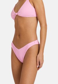 Roza rebrovani bikini komplet, ki vključuje trikotno zgornji del s vozlom in nizkoklesne spodnji del z gladkimi robovi. Mehek material, minimalen dizajn.