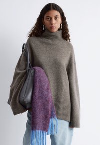 Beige übergroßer Rollkragenpullover mit gerippten Bündchen, kombiniert mit einem mehrfarbigen Schal in lila und blauen Tönen sowie einer schwarzen Handtasche.