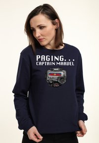 Felpa blu navy con la scritta "PAGING... CAPTAIN MARVEL" e un design grafico di un dispositivo tecnico con accenti rossi e blu.
